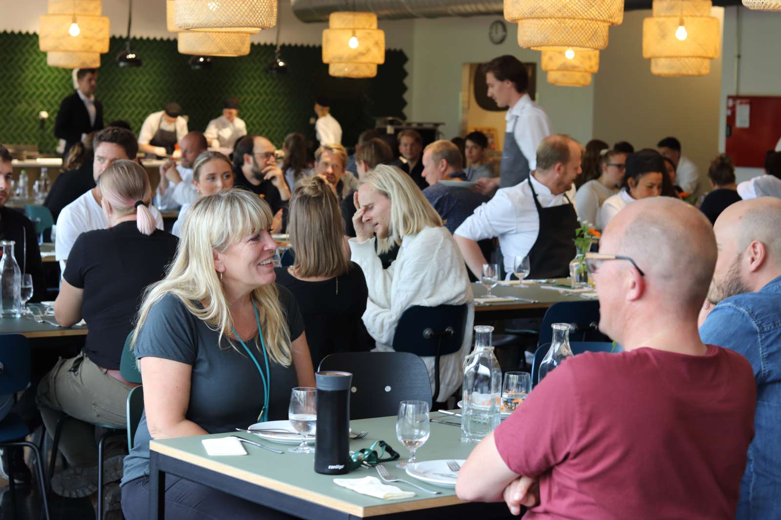 Medarbejdere på Hotel- og Restaurantskolen taler og griner ved langborde til stor fællesmiddag