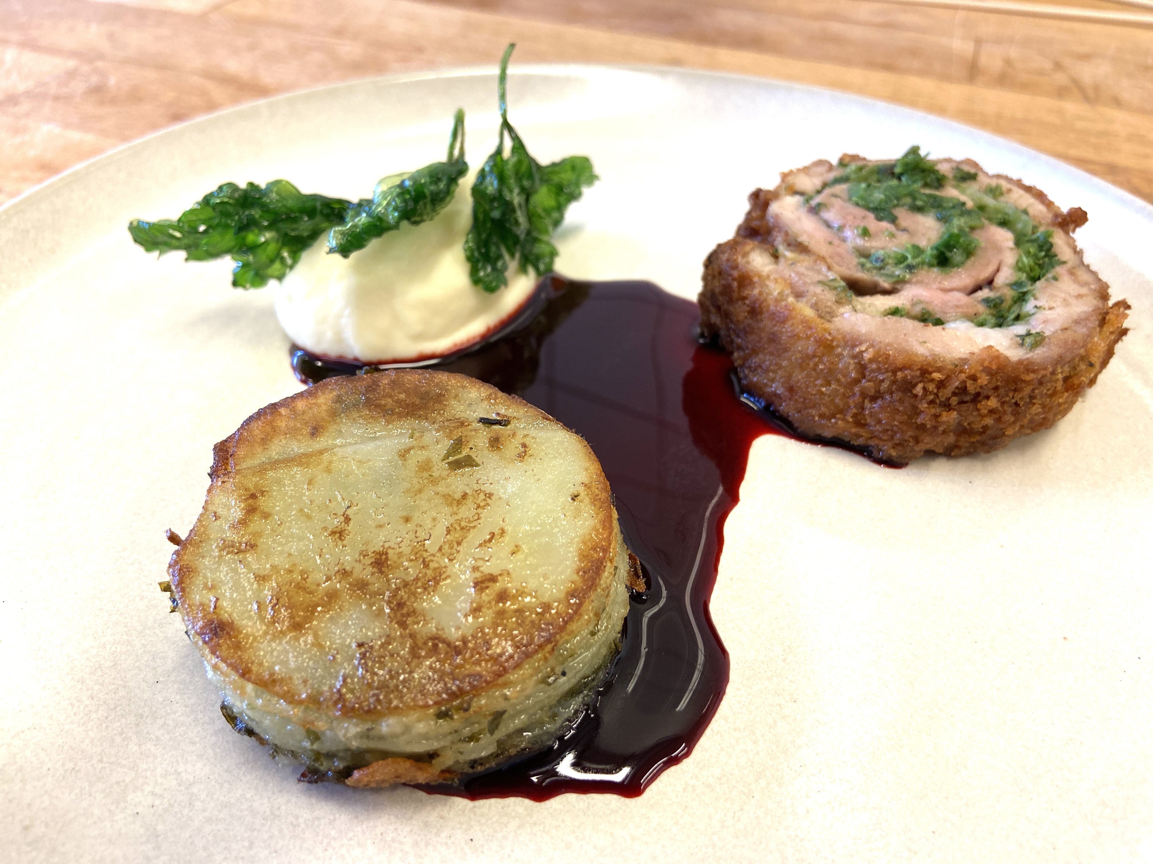 Ballotine af gris paneret med flæskesvær og serveret med pommes anna, seleripuré og rødbedeglace